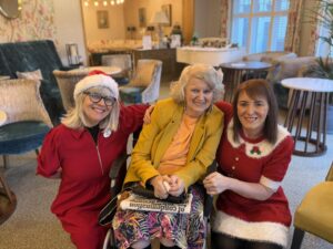 Two women dressed in santa outfits sit either sided of a resident at Cavendish Park Care Home in Evesham.