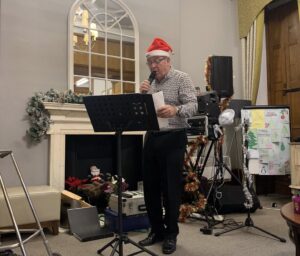 A man wearing a santa hat is singing at Milton Ernest Hall in Bedfordshire.