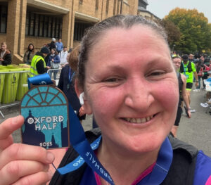 a woman smiling and holding up an oxford half marathon medal.